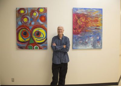 mendoza posing and smiling in front of his paintings