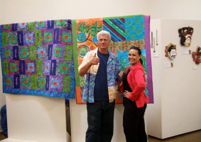 mendoza posing with a woman in front of his artworks