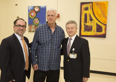 george mendoza posing in front of his paintings with two people