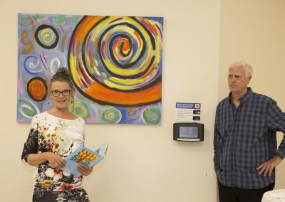 mendoza posed in front of his artwork and a woman holding his book