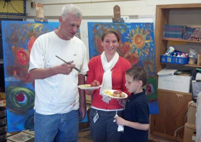 mendoza holding a paintbrush with a woman and two children in front of his paintings