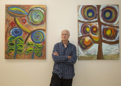 mendoza with his arms crossed posed in front of his paintings